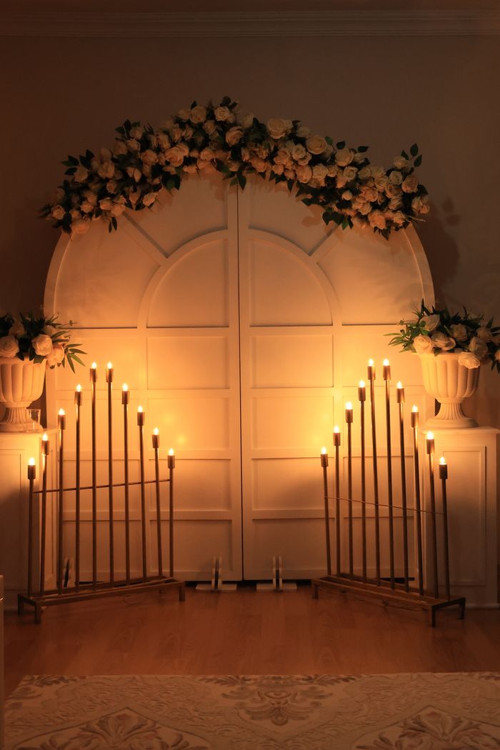 Warm and elegant candlelit wedding backdrop with flowers and archway.